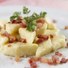 Kopytka z chrupiącym boczkiem i natką pietruszki, posypane pieprzem. Pyszne danie obiadowe.