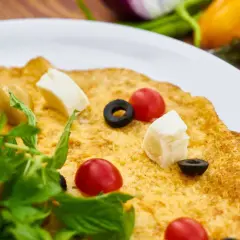 Pyszny omlet wytrawny z pomidorkami koktajlowymi, oliwkami i serem feta, udekorowany świeżą rukolą.