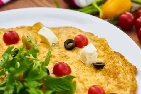 Pyszny omlet wytrawny z pomidorkami koktajlowymi, oliwkami i serem feta, udekorowany świeżą rukolą.