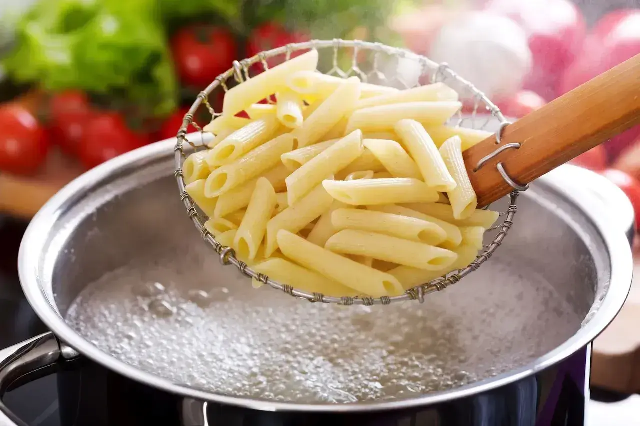 Penne prosto z gotowania, idealnie makaron al dente, unoszone nad bulgoczącą wodą.