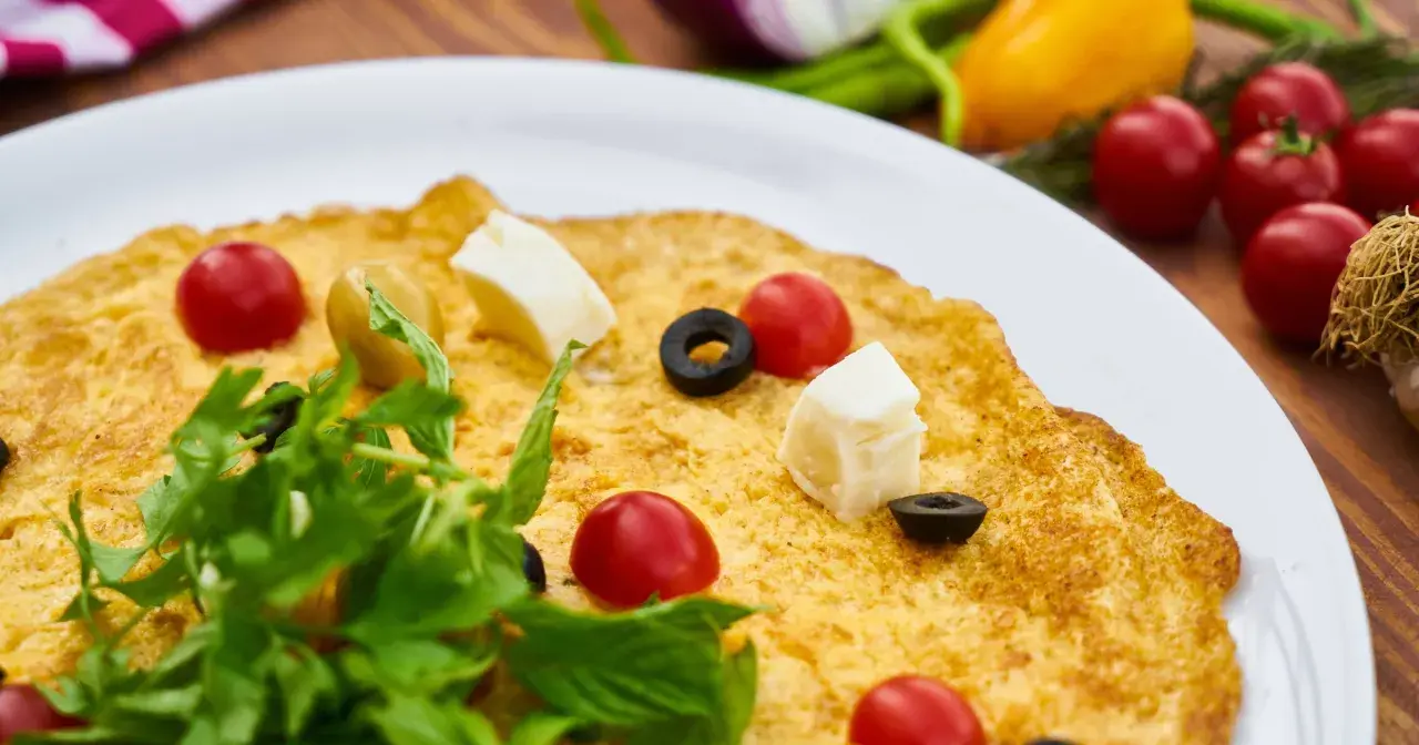 Pyszny omlet wytrawny z pomidorkami koktajlowymi, oliwkami i serem feta, udekorowany świeżą rukolą.
