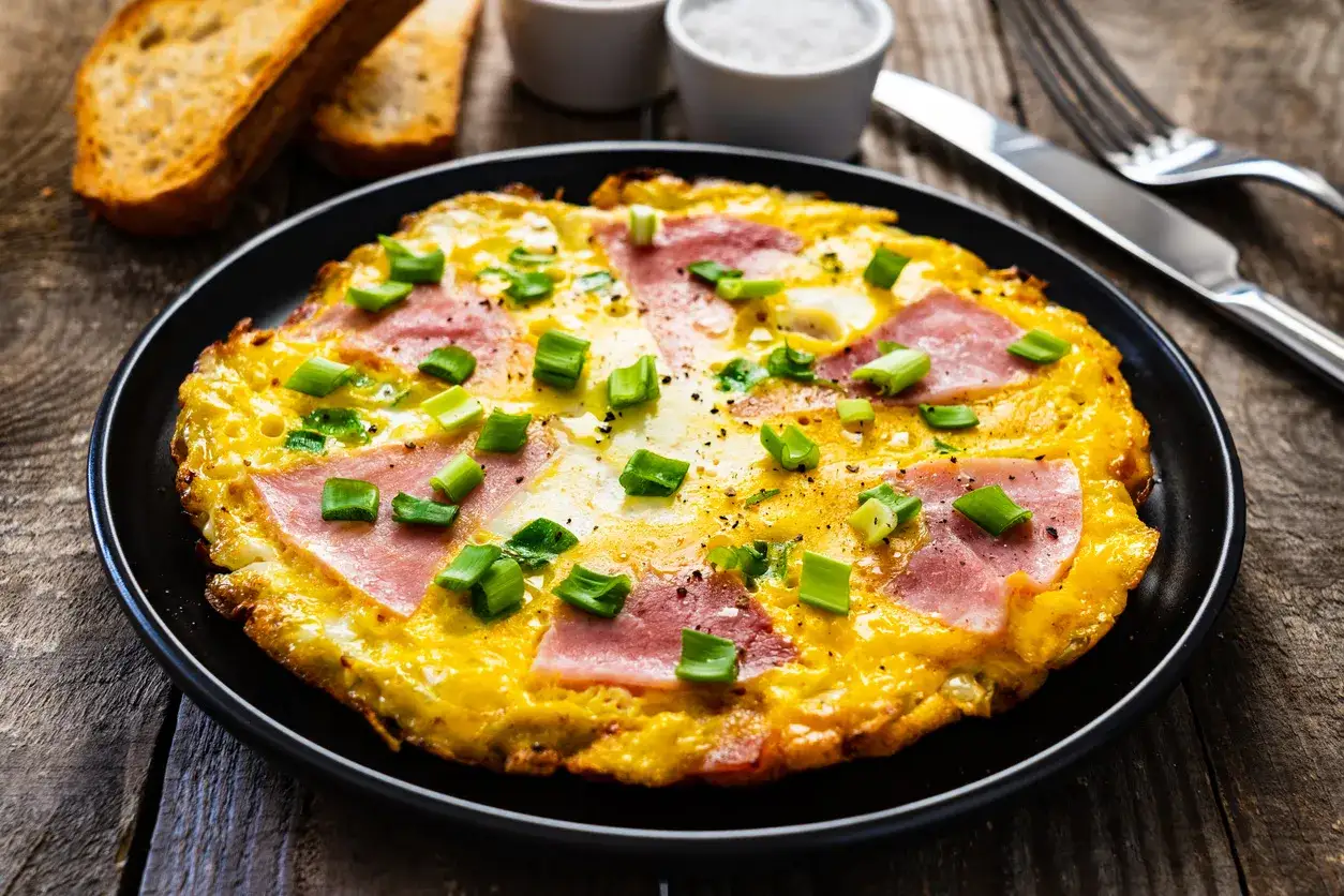 Pyszny omlet wytrawny z szynką i szczypiorkiem, podany z grzankami. Idealny na śniadanie.