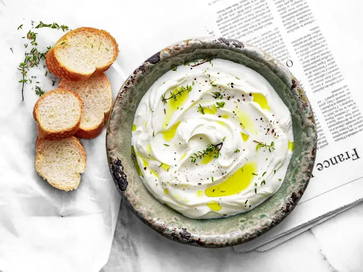 Labneh co to? Kremowy ser jogurtowy w misce, skropiony oliwą i ziołami, podany z kromkami bagietki.