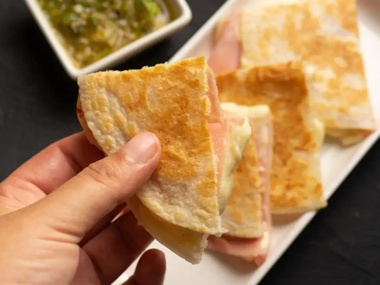 Chrupiące quesadille z szynką i serem, idealne na szybką kolację z niczego. Obok miseczka z zielonym sosem.