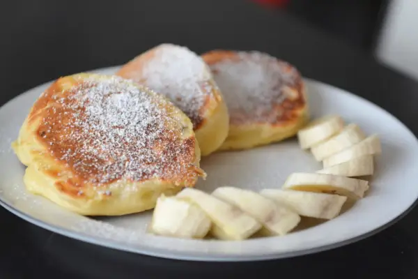 Szybkie placuszki na śniadanie, posypane cukrem pudrem, z kawałkami banana. Idealne na poranny posiłek.